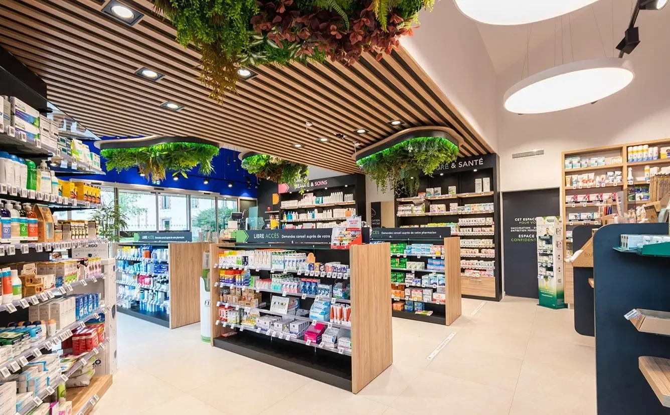Intérieur d’une officine moderne : rayonnages en bois, espaces de conseil et plantes suspendues